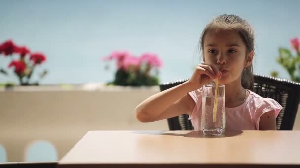 Kind is drinkwater in het restaurant dat aan de oever ligt — Stockvideo