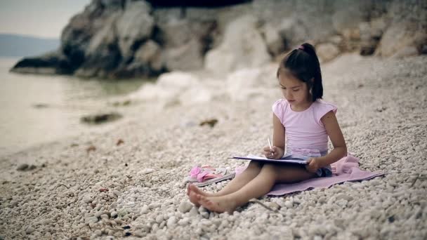 Un enfant est assis sur une pierre près de la mer Adriatique et dessine un tableau .