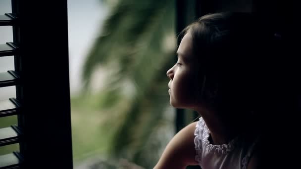 ? hild sitter på fönsterbrädan och tittar ut genom fönstret. — Stockvideo