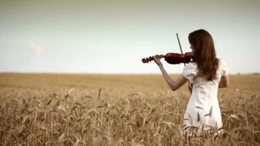 Kız kemancı buğday alanında keman çalıyor.