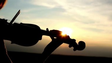 Siluet kız kemancı günbatımı gökyüzü arka plan keman çalıyor. Renk v.1