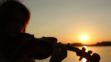 Kadın kemancı keman gölde gün batımında çalıyor.