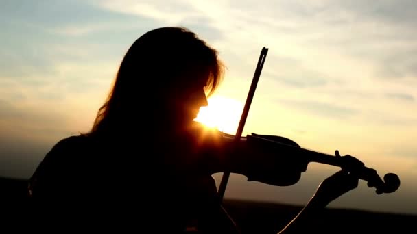 Violoniste fille silhouette jouant du violon au coucher du soleil fond du ciel. Couleur v.1 — Video