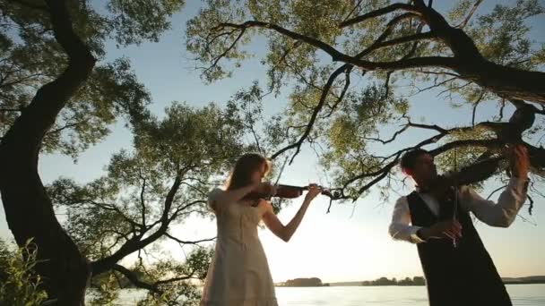 Скрипичный дуэт мужчина и женщина играют на скрипке на природе на закате на озере — стоковое видео