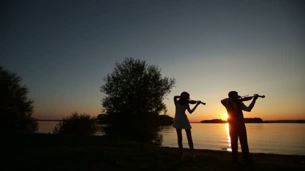 Hegedű Duett férfi és nő hegedülni a természet a naplementekor a tavon