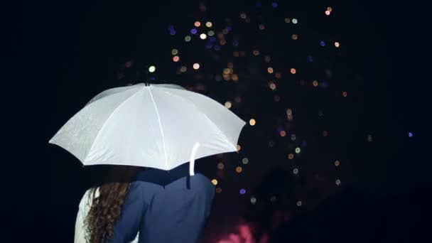 La gente se para bajo un paraguas y ve fuegos artificiales. . — Vídeo de stock