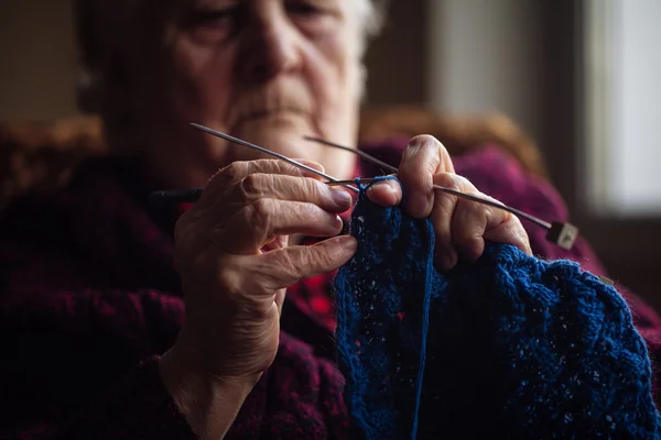 De oude vrouw zit thuis en breit kleding — Stockfoto