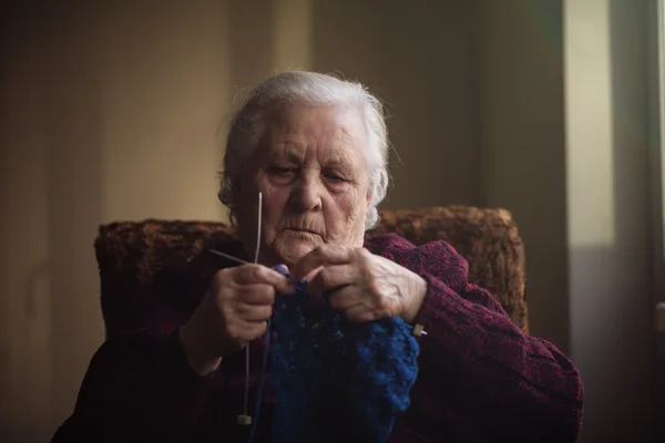 Wanita tua itu duduk di rumah dan merajut pakaian — Stok Foto