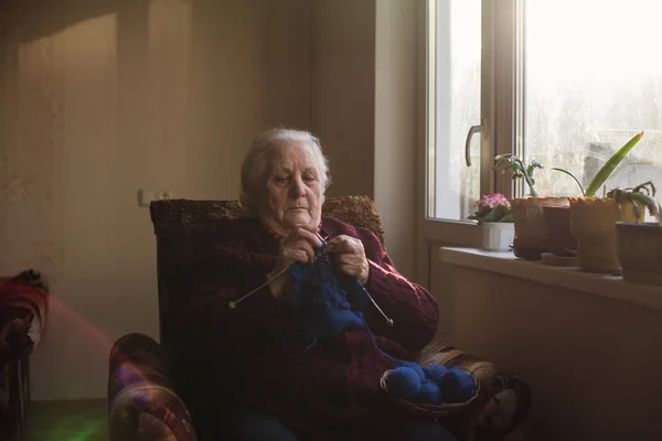Die alte Frau sitzt zu Hause und strickt Kleidungsstücke — Stockfoto