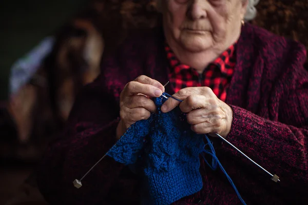 De oude vrouw zit thuis en breit kleding — Stockfoto