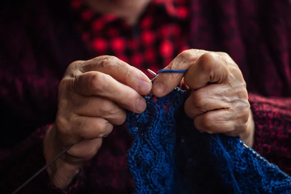 A velha senta-se em casa e tricota roupas . — Fotografia de Stock