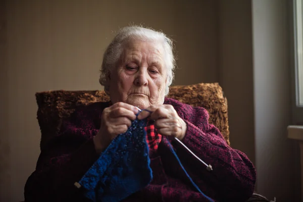 A velha senta-se em casa e tricota roupas — Fotografia de Stock