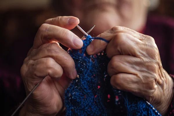 La anciana se sienta en casa y teje prendas . — Foto de Stock