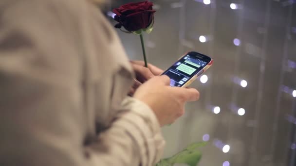 La chica con una rosa en la mano utiliza una chica de teléfono escribe su mensaje de novio . — Vídeo de stock