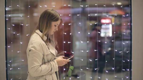 La chica con una rosa en la mano utiliza una chica de teléfono escribe su mensaje de novio . — Vídeos de Stock