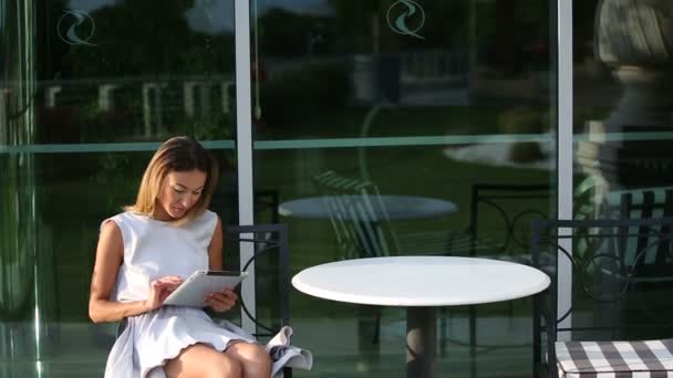 Joven mujer de negocios hermosa sentada en una mesa con la tableta en las manos — Vídeo de stock