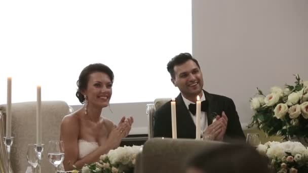 Recién casados en la boda sentados a la mesa para un festivo aplaudido y sonriente — Vídeo de stock