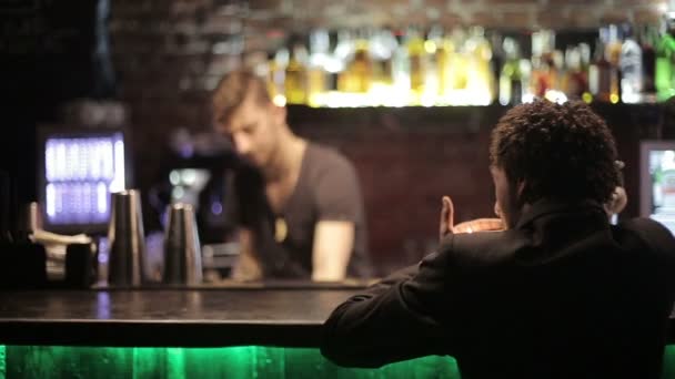 En svart man sitter på en bar och röker en cigarett — Stockvideo