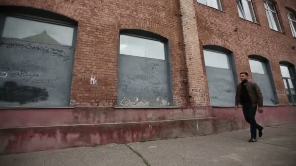 Успешный счастливый человек идет на фоне кирпичной стены старой фабрики — стоковое видео