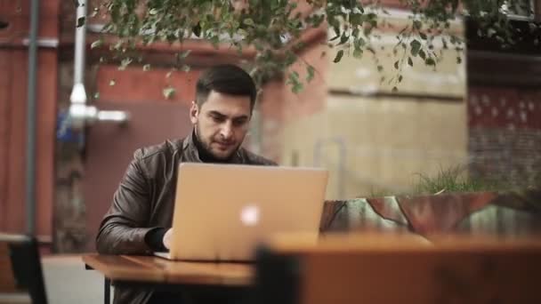 Un hombre utiliza un ordenador portátil al aire libre . — Vídeos de Stock