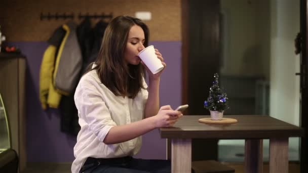 Chica joven bebiendo café y escribiendo SMS saludando a los amigos feliz año nuevo — Vídeos de Stock