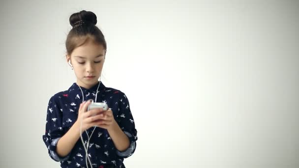 Niño utiliza teléfono inteligente con orejeras en el fondo del estudio — Vídeos de Stock