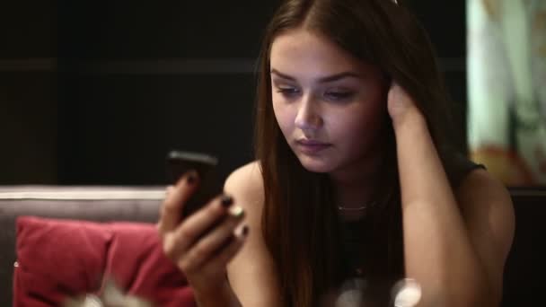 Una ragazza la sera in un caffè utilizzando lo smartphone — Video Stock