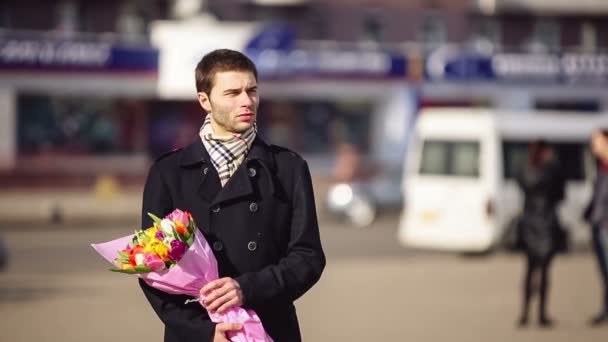 Мужчина с цветами ждет свою женщину в городе — стоковое видео