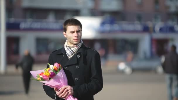 Мужчина с цветами ждет свою женщину в городе — стоковое видео