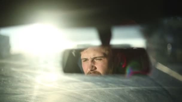 Un hombre conduce un coche. Cara de reflexión en el espejo retrovisor del coche. Tiempo de puesta del sol — Vídeos de Stock