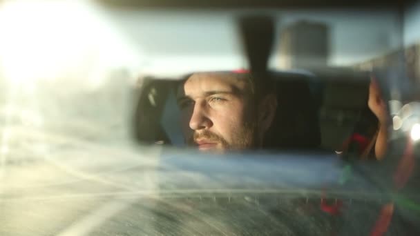 Мужчина водит машину. Отражение лица в зеркале заднего вида автомобиля. Время заката — стоковое видео