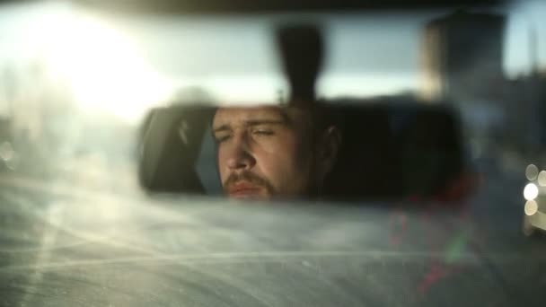 Een man rijdt een auto. Reflectie gezicht in de achteruitkijkspiegel van de auto. Zonsondergang tijd — Stockvideo