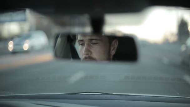 Un hombre conduce un coche. Cara de reflexión en el espejo retrovisor del coche. Tiempo de puesta del sol — Vídeos de Stock