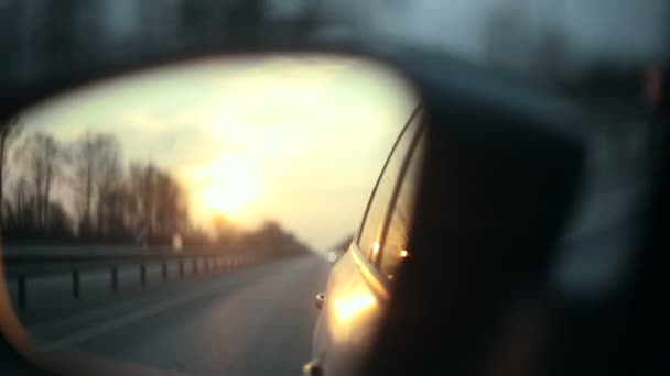 Вид на дорогу в зеркале заднего вида автомобиля на закате — стоковое видео