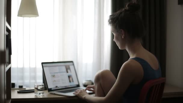 Mujer joven trabaja con el ordenador portátil en una habitación de hotel por la mañana — Vídeo de stock