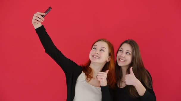 Chicas tomando autorretrato con el teléfono inteligente ver fotos sonrisa y reír. En cámara lenta. Fondo de estudio rojo — Vídeos de Stock