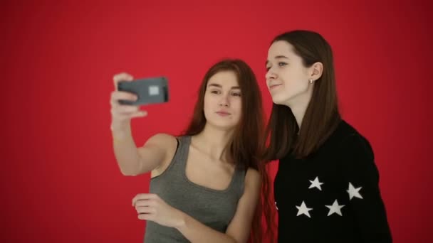 Chicas tomando autorretrato con el teléfono inteligente ver fotos sonrisa y reír. Fondo de estudio rojo — Vídeos de Stock
