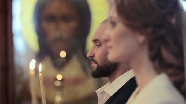 Cerrar pareja de boda en una iglesia con velas en Jesucristo icono de fondo — Vídeo de stock