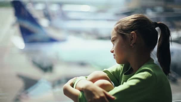 Kind op het vliegveld bij het raam kijkend naar vliegtuigen en wachtend op de tijd van de vlucht — Stockvideo