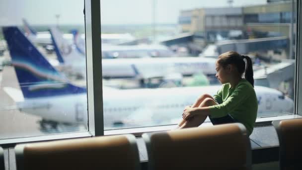 Dziecko na lotnisku przy oknie patrzące na samoloty i czekające na czas lotu — Wideo stockowe