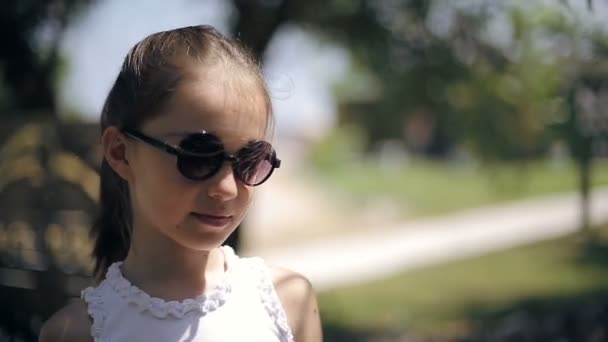 Criança feminina atraente em óculos de sol sorrindo e rindo na natureza — Vídeo de Stock