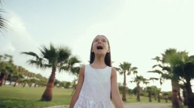 Çocuk bir palm sokaktan batımında yürüyüşler, sevinir ve şarkı söylüyor