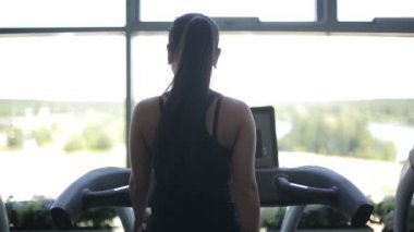 Koşu bandı üzerinde çalışan ve büyük penceresine bakarak çekici Asyalı kız
