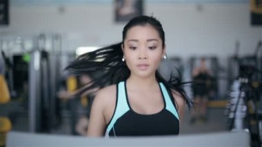 Spor salonunda treadmill çalıştıran çekici Asyalı kız. Tam yüz portre
