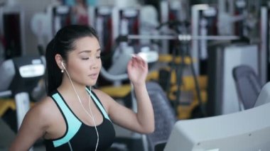 Kulaklık ile spor salonunda treadmill çalıştıran çekici Asyalı kız. Doğru profil yüz