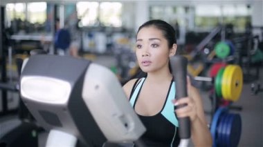 Çekici Asyalı kız jimnastik salonunda XTrainer makinesinde egzersiz yapıyor.