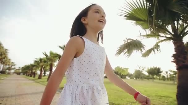 Kind loopt door een palm steegje bij zonsondergang, verheugt zich en zingt — Stockvideo