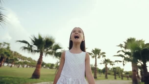 Child walks through a palm alley at sunset, rejoices and sings — Stock Video