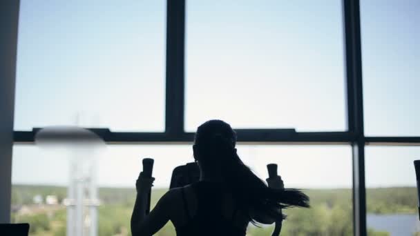 Silhouet van aantrekkelijke jonge vrouw op de sportschool uit te oefenen op de xtrainer machine — Stockvideo