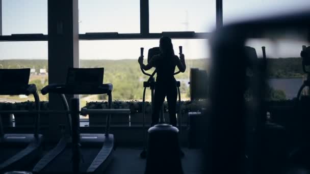 Silueta de mujer joven atractiva en el gimnasio haciendo ejercicio en la máquina xtrainer — Vídeo de stock